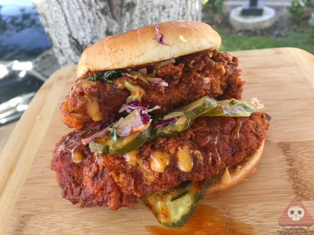 Dave's Hot Chicken Slider with two pieces of hot chicken pickles and slaw on a cutting board